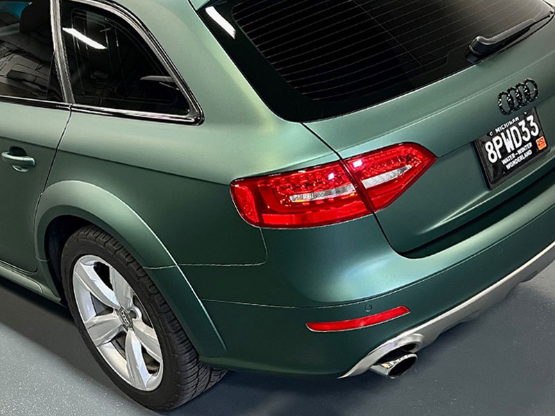 Rear view of a green Audi car with visible taillight, license plate, and silver wheels, parked indoors.