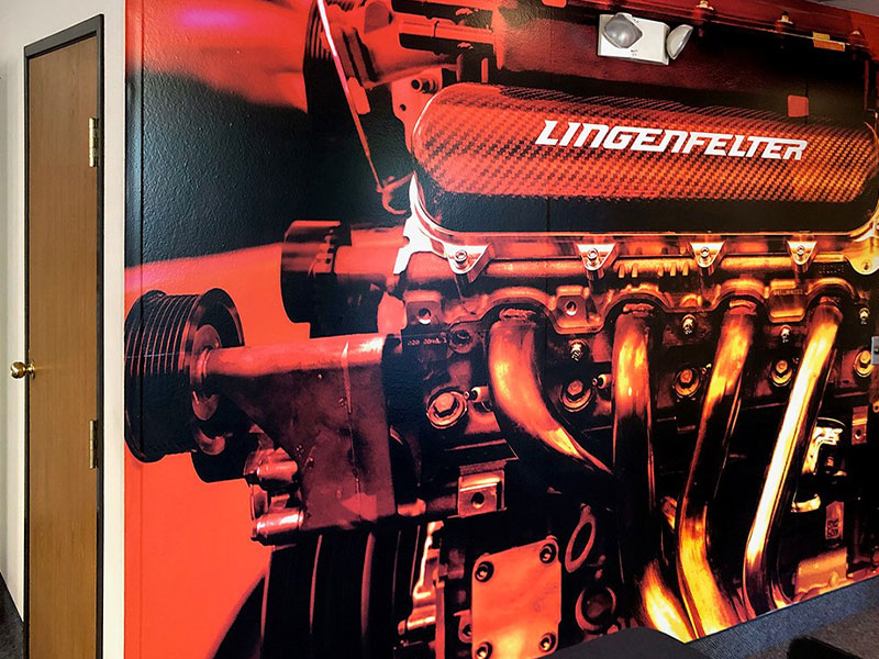 Wall mural featuring a detailed image of a Lingenfelter engine in red and orange tones next to a wooden door.
